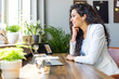 © Dragana Gordic - Cheerful young businesswoman having a video call in a modern co-working space. Happy female entrepreneur communicating with her business associates while working remotely.
