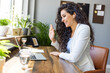 © Dragana Gordic - Focused young businesswoman using a laptop and wireless earphones while working alone. Young female entrepreneur working remotely in a modern co-working office.