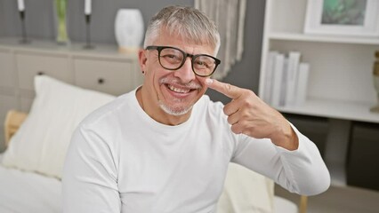 Sticker - Charming middle age grey-haired man in pyjamas demonstrates beauty care. smiling, he points a finger to his clean face and nose, truly happy in his cosy bedroom.