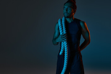 attractive young african american man in sport uniform holding battle rope and looking away