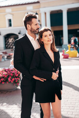 Wall Mural - Beautiful fashion woman and her handsome elegant boyfriend in black suit. Sexy brunette model in jacket. Fashionable confident couple posing in street. Brutal man and female outdoors