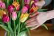 closeup of florists hands arranging tulips in a vase