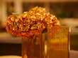 Artificial flowers stand in a decorative orange glass vase on a wooden table