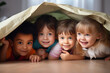 Group of happy children hiding under a blanket in the room at home