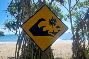 Yellow tsunami warning sign with pandanus plants on the beach.