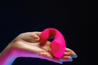 In the palm of the girl's hand is a sex toy from a sex shop. Sex toy clitoral vibrator on a black background with neon lights.
