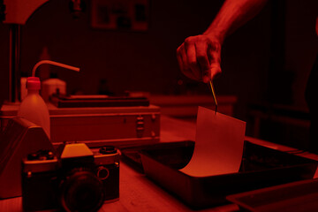 cropped shot of young man delicately immerses photo paper in a darkroom bath with chemicals