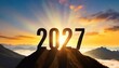 Year 2027, concept. New Year 2027 at sunset. Silhouette 2027 stands on a mountain with sun rays at sunrise, creative idea	
