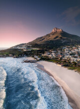 Aerial View Of Lions Head Mountain At Sunset With A Pink Horizon, White Sandy Beach, And Blue Waves Rolling Onto Shore, Cape Town, Western Cape, South Africa.