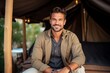 Portrait of a handsome young man sitting in a tent smiling at the camera