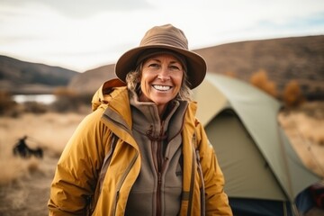 Wall Mural - Portrait of smiling senior woman in yellow jacket and hat standing near camping tent