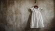 Elegant white dress for little girl's christening, hanging on the wall using a wooden hanger