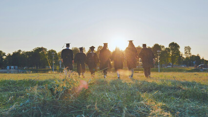 Wall Mural - Graduate students walking through an evening meadow at sunset.