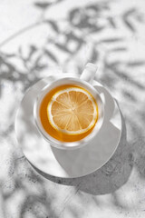 Wall Mural - A cup of tea with lemon on a white table with flower shadow. Breakfast concept.