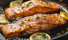 Close-up Of Salmon Fillets Sizzling In A Frying Pan With Slices Of Lemon And Fresh Herbs, Creating An Appetizing And Flavorful Cooking Scene