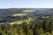 Malerische Landschaft in der Eifel mit grünen Hügeln, einem kleinen Dorf und Windräder im Hintergrund. 