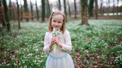 Wall Mural - Cute preschooler girl in green tutu skirt gathering snowdrop flowers in park or forest on a spring day. Little kid exploring nature. Outdoor activities for children