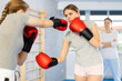 Two teenage girls in boxing gloves learn to box under guidance of trainer in the gym