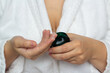© brajianni - Young white woman in bathrobe with neckline takes out moisturizing cosmetic cream from green glass jar closeup in hotel bedroom. Skin protection during cold season. Cosmetic procedure in spa salon