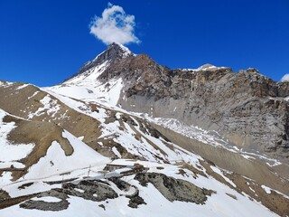 Snowy mountain stands tall amidst white landscape, as a lone cloud floats lazily in the bright blue sky.