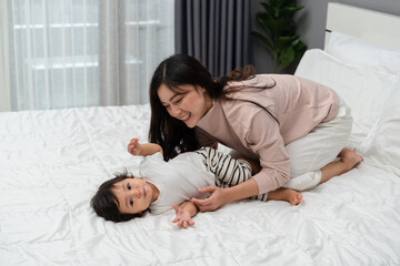 Wall Mural - happy mother lying and playing with her infant baby on bed