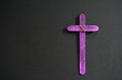 A purple wooden cross in black background. Christian faith, holy week or lent season celebration concept.