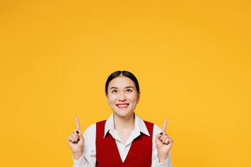 Wall Mural - Young fun corporate lawyer employee business woman of Asian ethnicity wear formal red vest shirt work at office point index finger overhead on area isolated on plain yellow background. Career concept.