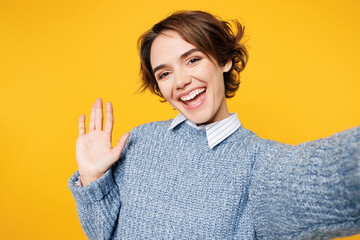 Wall Mural - Close up young woman she wears grey knitted sweater shirt casual clothes doing selfie shot pov on mobile cell phone waving hand isolated on plain yellow background studio portrait. Lifestyle concept.