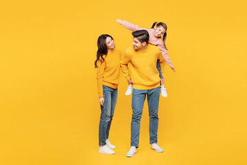 Poster - Full body young joyful parents mom dad with child kid girl 7-8 years old wear pink sweater casual clothes giving piggyback ride, sitting on back isolated on plain yellow background Family day concept