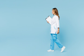 Wall Mural - Full body side view female doctor woman wear white gown suit work in hospital clinic office holding clipboard with medical documents go isolated on plain blue background. Health care medicine concept.