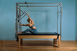 © Georgii - Young girl doing pilates exercises with a reformer bed. Beautiful slim fitness trainer on reformer gray background, low key, art light. Fitness concept