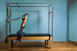 © Georgii - Young girl doing pilates exercises with a reformer bed. Beautiful slim fitness trainer on reformer gray background, low key, art light. Fitness concept