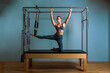 © Georgii - Young girl doing pilates exercises with a reformer bed. Beautiful slim fitness trainer on reformer gray background, low key, art light. Fitness concept