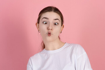 Wall Mural - Portrait of attractive Caucasian young brunette woman with funny face wearing casual white t-shirt isolated on pink studio background.