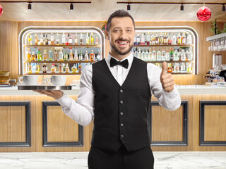 Poster - Waiter holding a tray with coffee cups and showing thumbs up at a bar