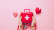© Kowit - Hands presenting a first aid kit with a red stethoscope and heart shapes on a pink background, symbolizing healthcare.
