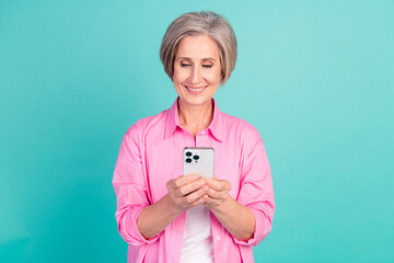 Poster - Portrait of cheerful smart woman with white gray hairdo dressed stylish shirt look at smartphone isolated on teal color background