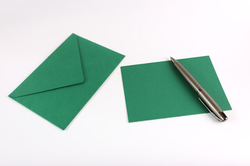 A green envelope, a sheet of paper and a pen on a white background.