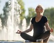 Mature sportswoman meditating while sitting against fountain at park