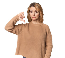 Blonde middle-aged Caucasian woman in studio showing a dislike gesture, thumbs down. Disagreement concept.