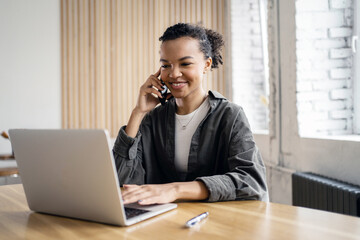 Young entrepreneur in casual attire multitasking with a laptop and a phone call.