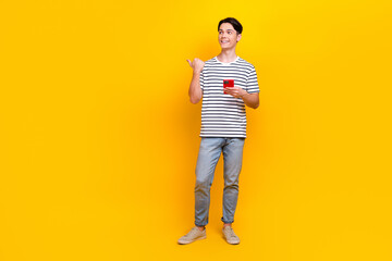 Poster - Full length photo of clever guy wear t-shirt look directing at promo empty space hold smartphone isolated on yellow color background