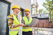 © LIGHTFIELD STUDIOS - cheerful bearded men in safety vests and helmets working with laptop on construction site, builders