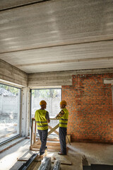 two hardworking bearded men in safety vests and helmets on construction site, cottage builders