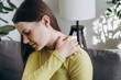 © Yura Yarema - Close up of unhappy sad young woman sitting on sofa suffering from pain in shoulder, doing self-massage. Neck pain. Forearm pain, people with body muscle problems, healthcare and medicine concept