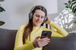 © Yura Yarema - Portrait of happy peaceful young caucasian woman hold phone relaxing on comfortable couch, listening to tranquil classical music in wireless headphones, enjoying lazy weekend hobby time alone at home