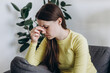 © Yura Yarema - Tired young lady unwell stressed headache suffer depression sitting on sofa at home. Upset woman head pain ache discomfort migraine overworked exhausted frustrated loneliness anxiety worried problem