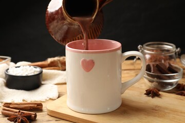 Poster - Pouring tasty hot chocolate into cup at wooden table, closeup