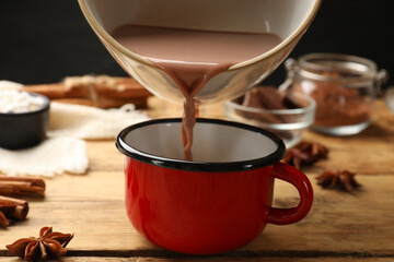 Wall Mural - Pouring tasty hot chocolate into cup at wooden table, closeup