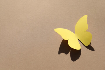 Wall Mural - Yellow paper butterfly on light brown background, above view. Space for text